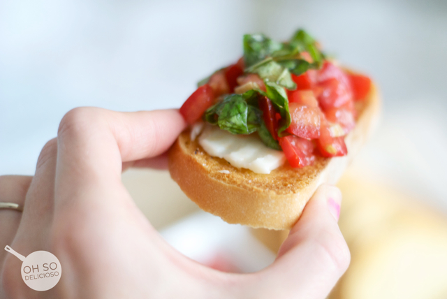 A slice of tomato bruschetta topped with tomatoes, parmesan and basil